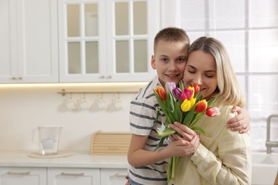 Photo of Happy Mother's Day. Son greeting his mom with flowers in kitchen. Space for text