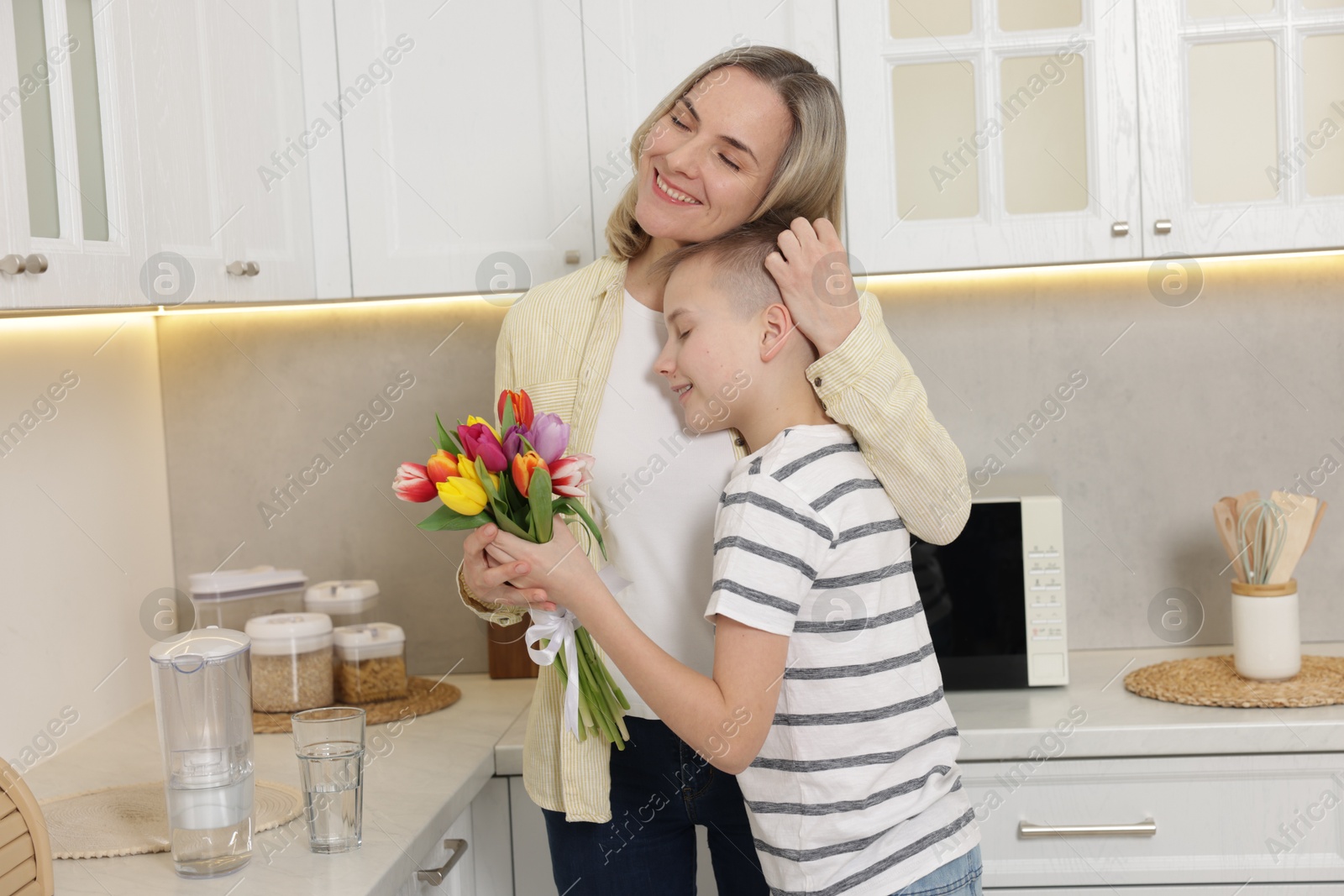 Photo of Happy Mother's Day. Son greeting his mom with flowers in kitchen