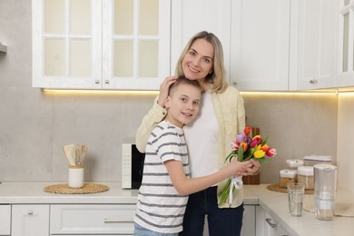 Photo of Happy Mother's Day. Son greeting his mom with flowers in kitchen. Space for text