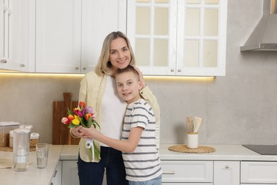 Photo of Happy Mother's Day. Son greeting his mom with flowers in kitchen. Space for text