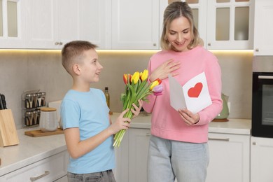 Photo of Happy Mother's Day. Son greeting his mom with flowers and card in kitchen