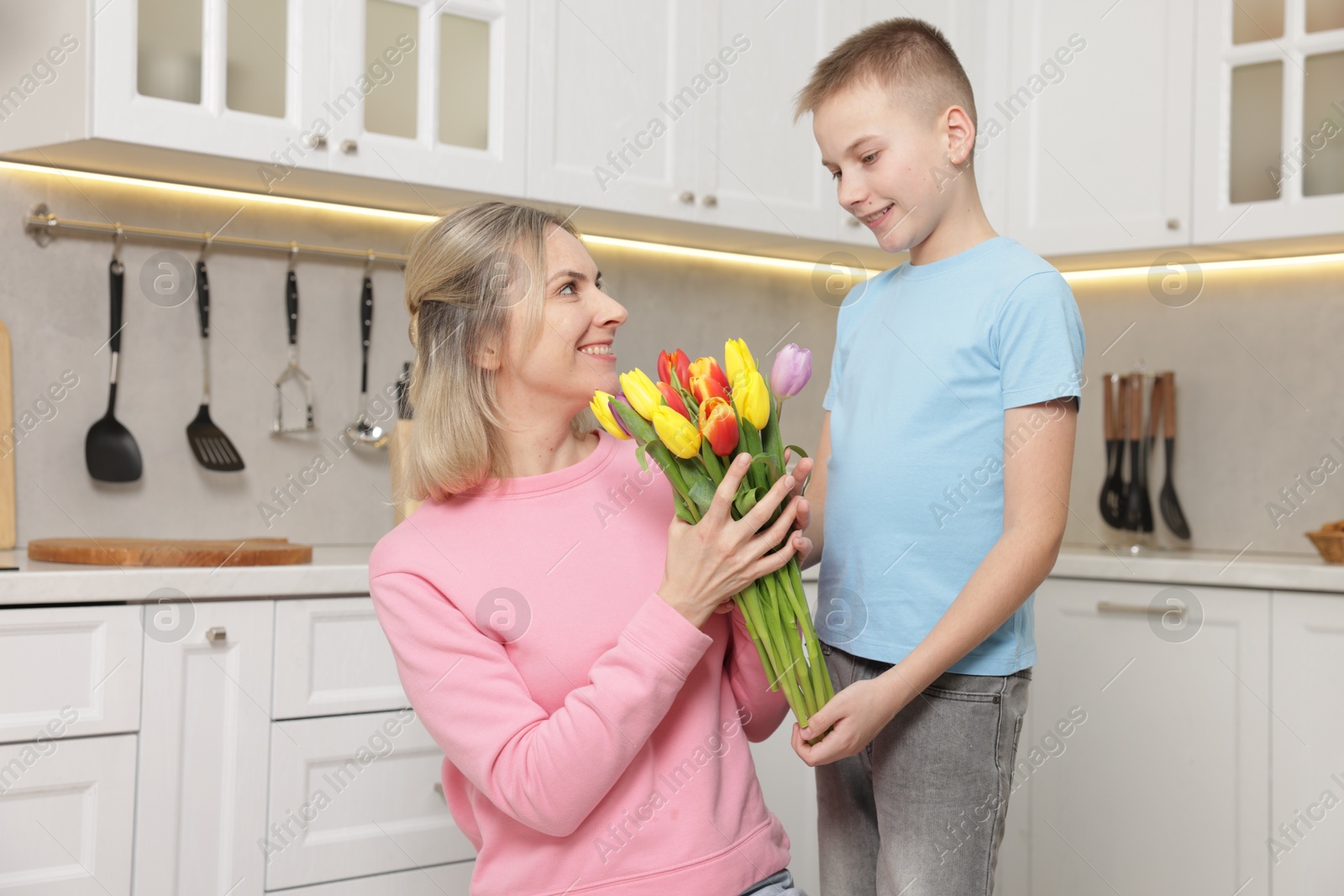 Photo of Happy Mother's Day. Son greeting his mom with flowers in kitchen