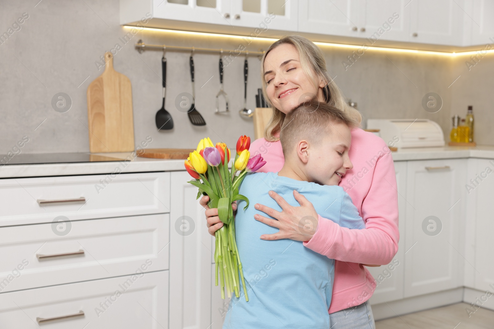 Photo of Happy Mother's Day. Son greeting his mom with flowers in kitchen