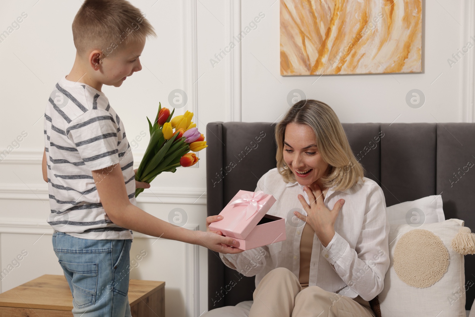 Photo of Happy Mother's Day. Son surprising his mom with gift and flowers at home