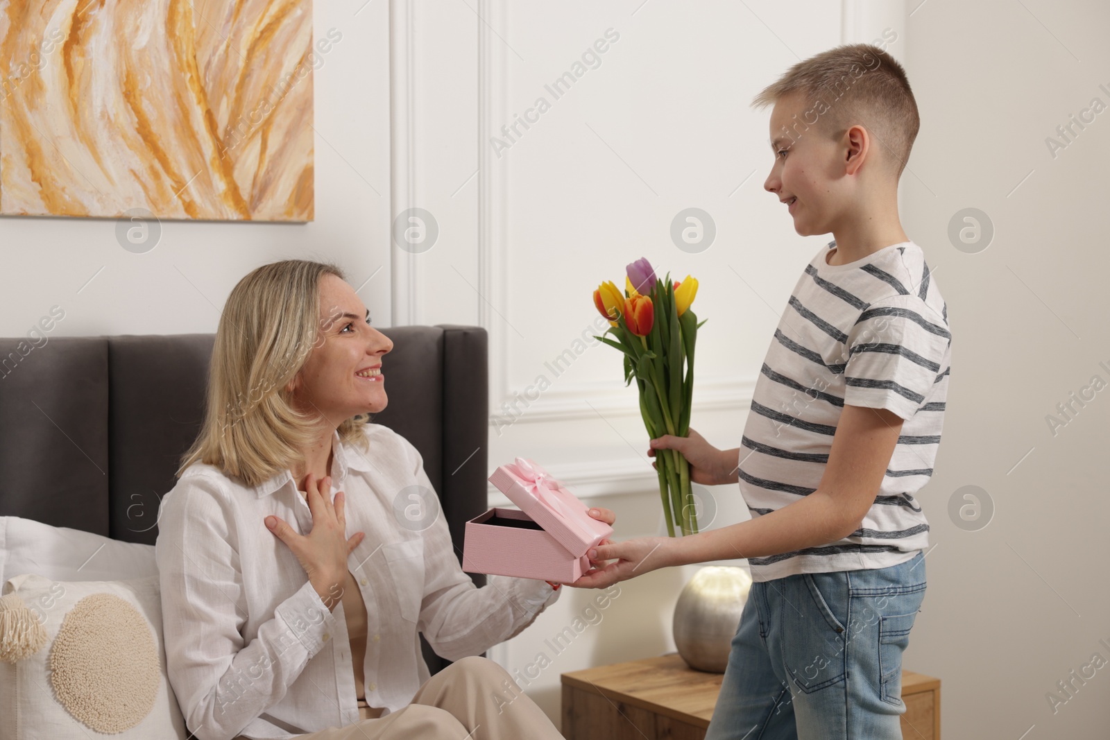 Photo of Happy Mother's Day. Son surprising his mom with gift and flowers at home