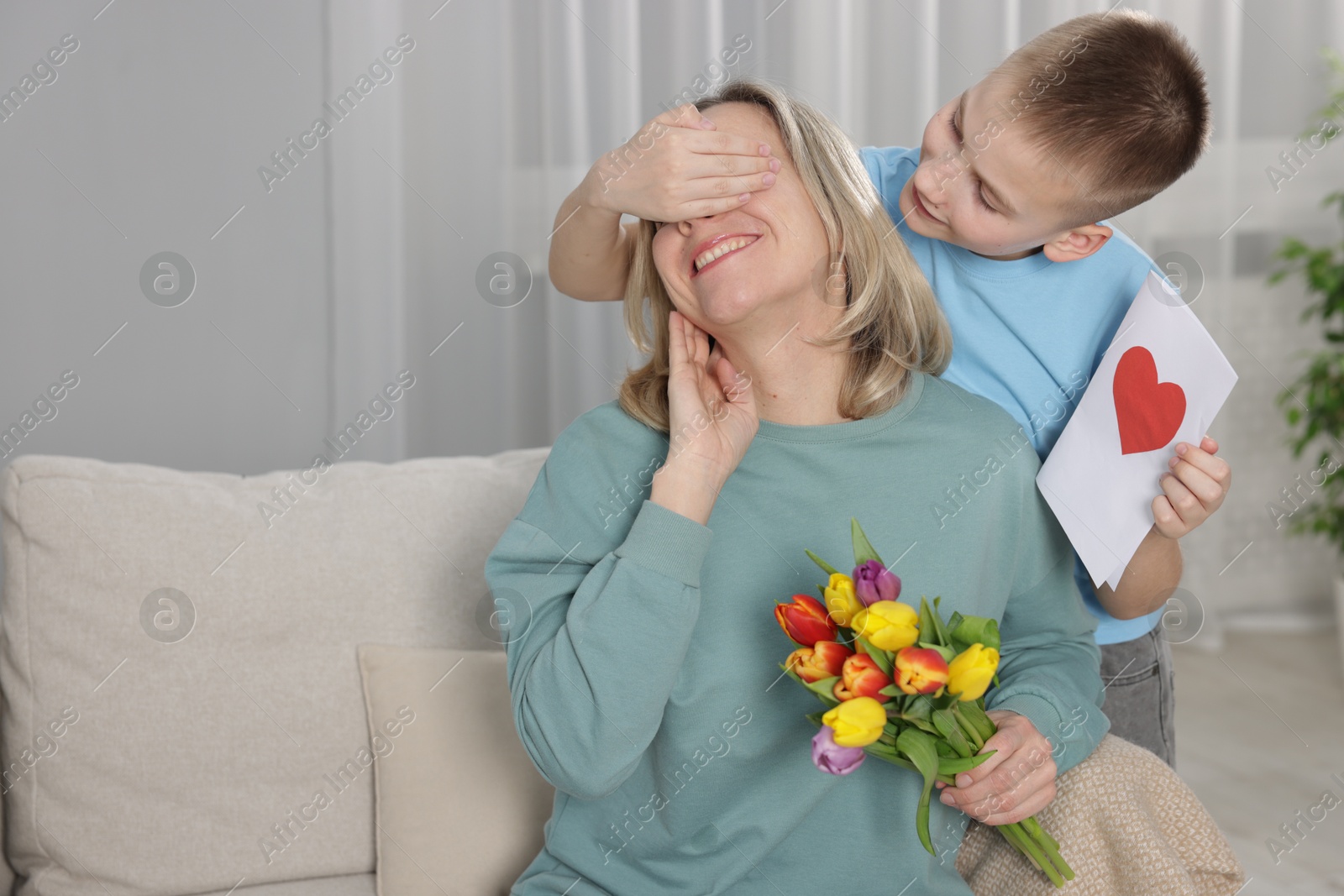 Photo of Happy Mother's Day. Son surprising his mom with flowers and card at home. Space for text