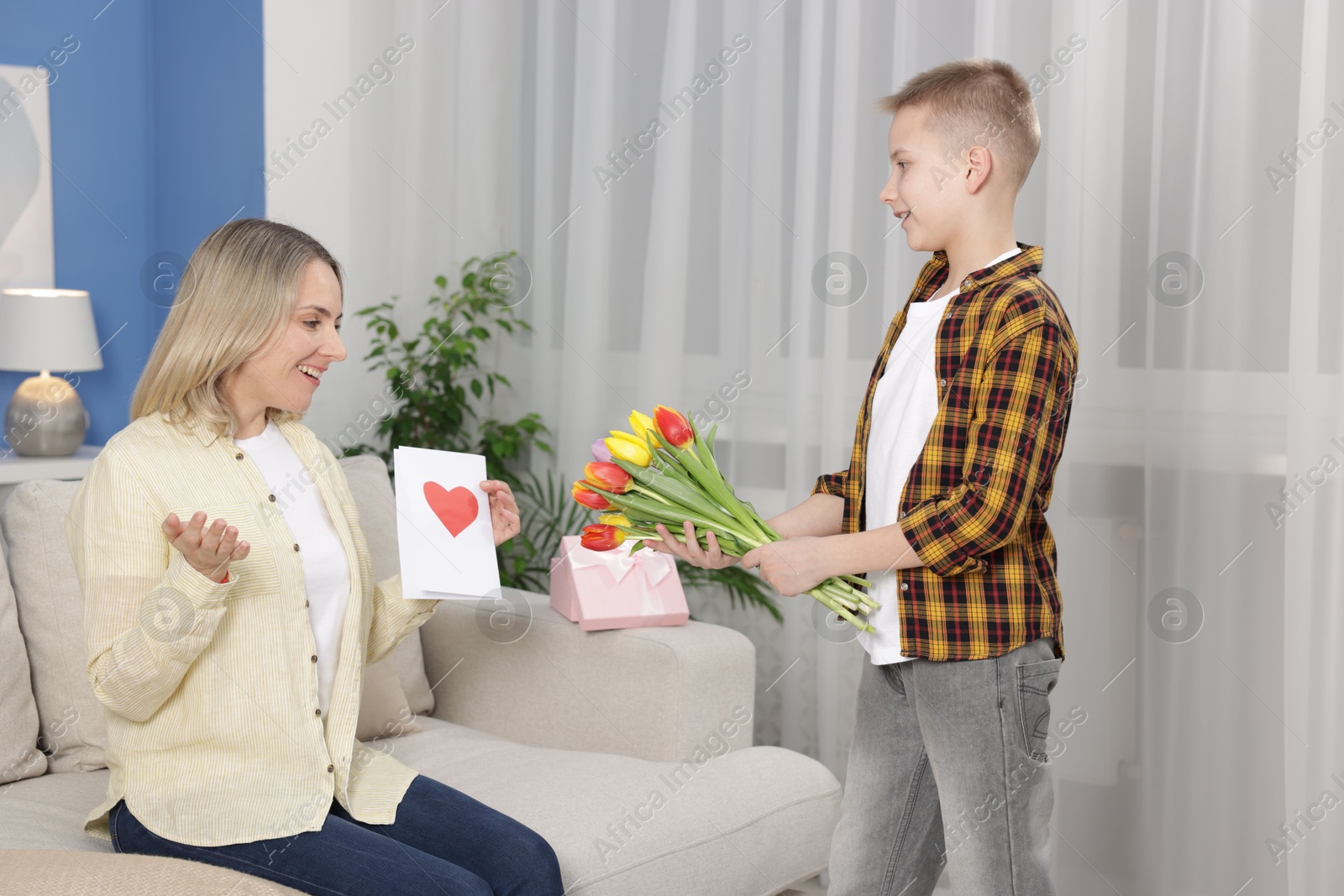 Photo of Happy Mother's Day. Son surprising his mom with flowers, gift and card at home