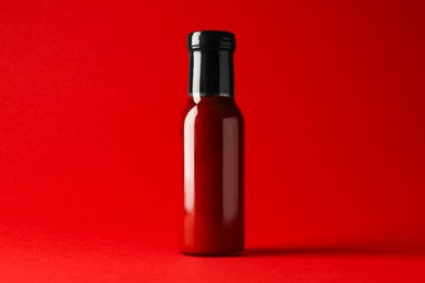 Photo of Ketchup in glass bottle on red background