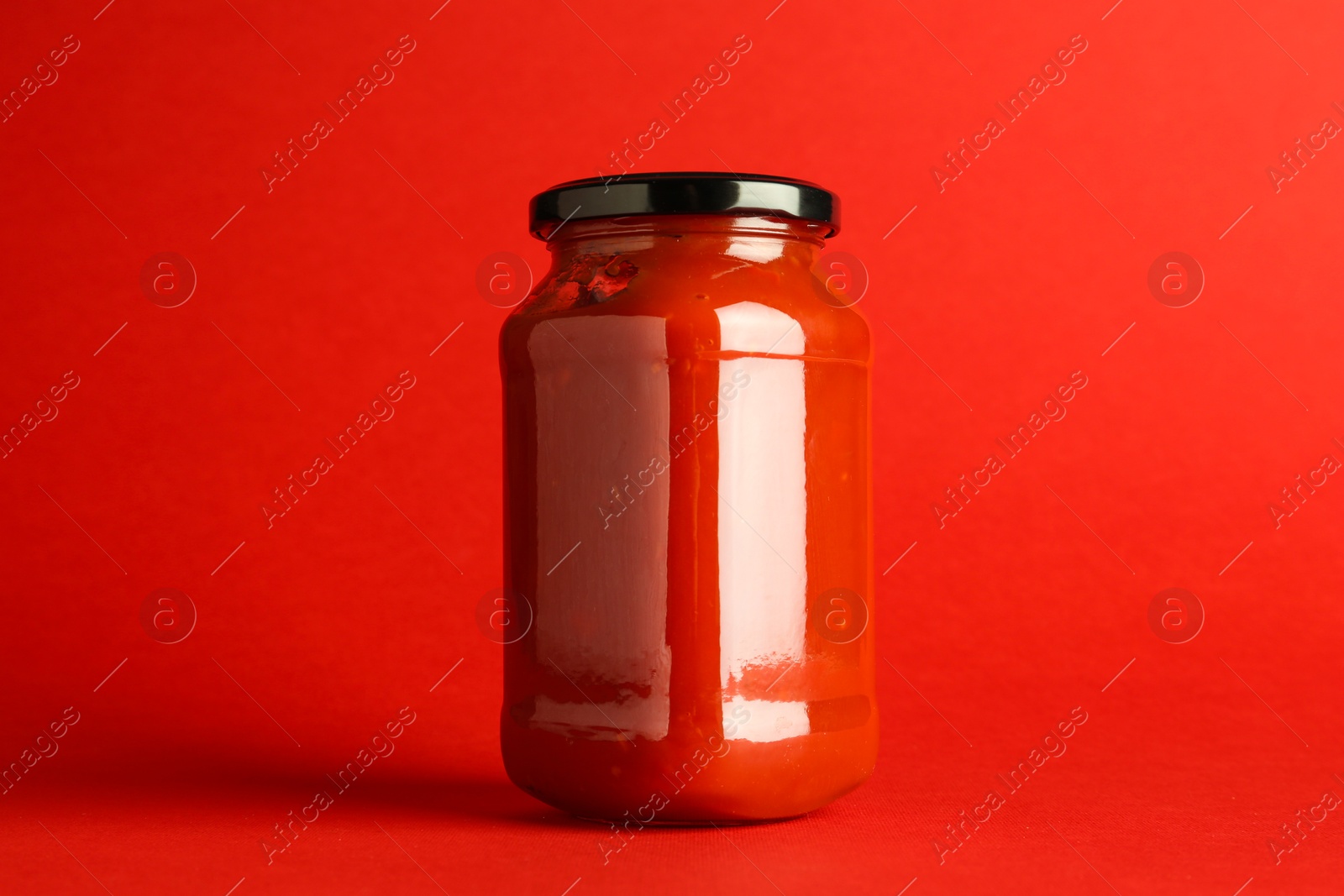 Photo of Ketchup in glass jar on red background