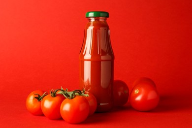 Photo of Ketchup in glass bottle and fresh tomatoes on red background