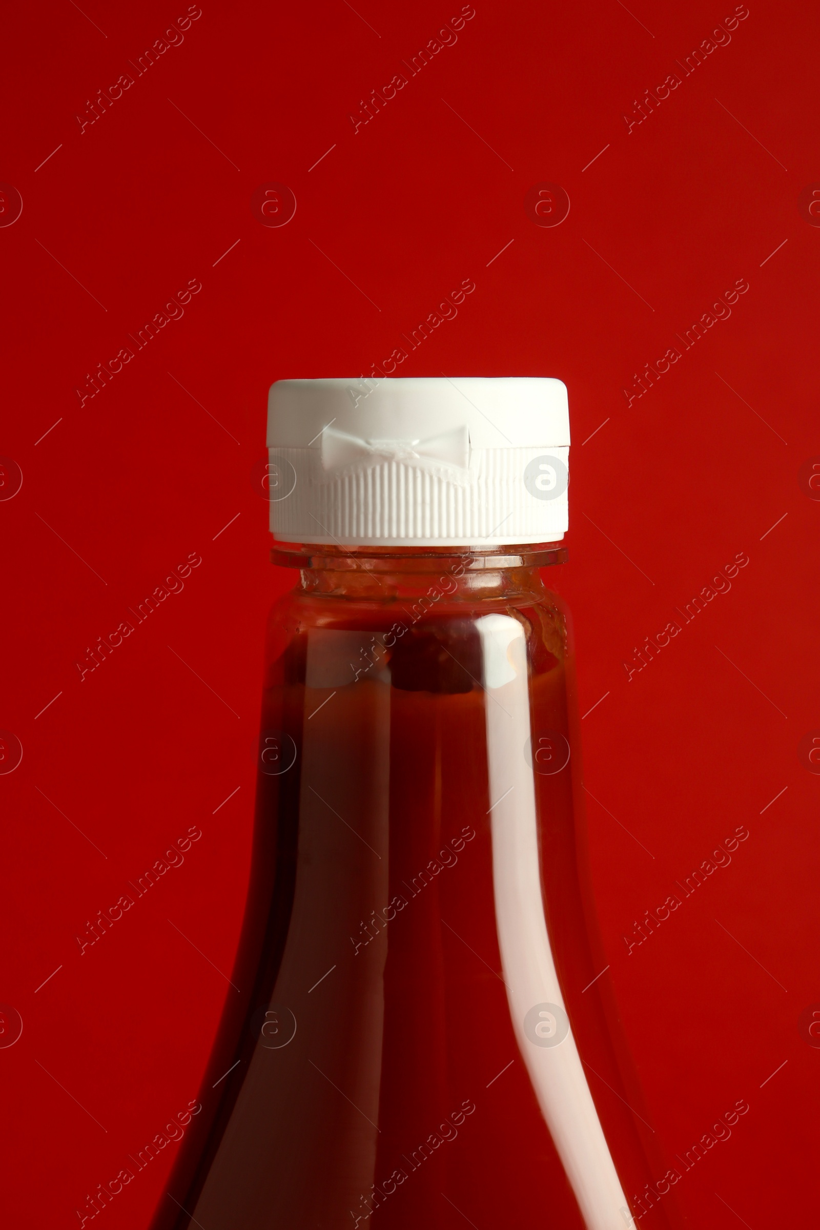 Photo of Tasty ketchup in bottle on red background, closeup