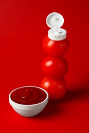 Photo of Stack of fresh tomatoes with plastic cap as bottle and ketchup in bowl on red background