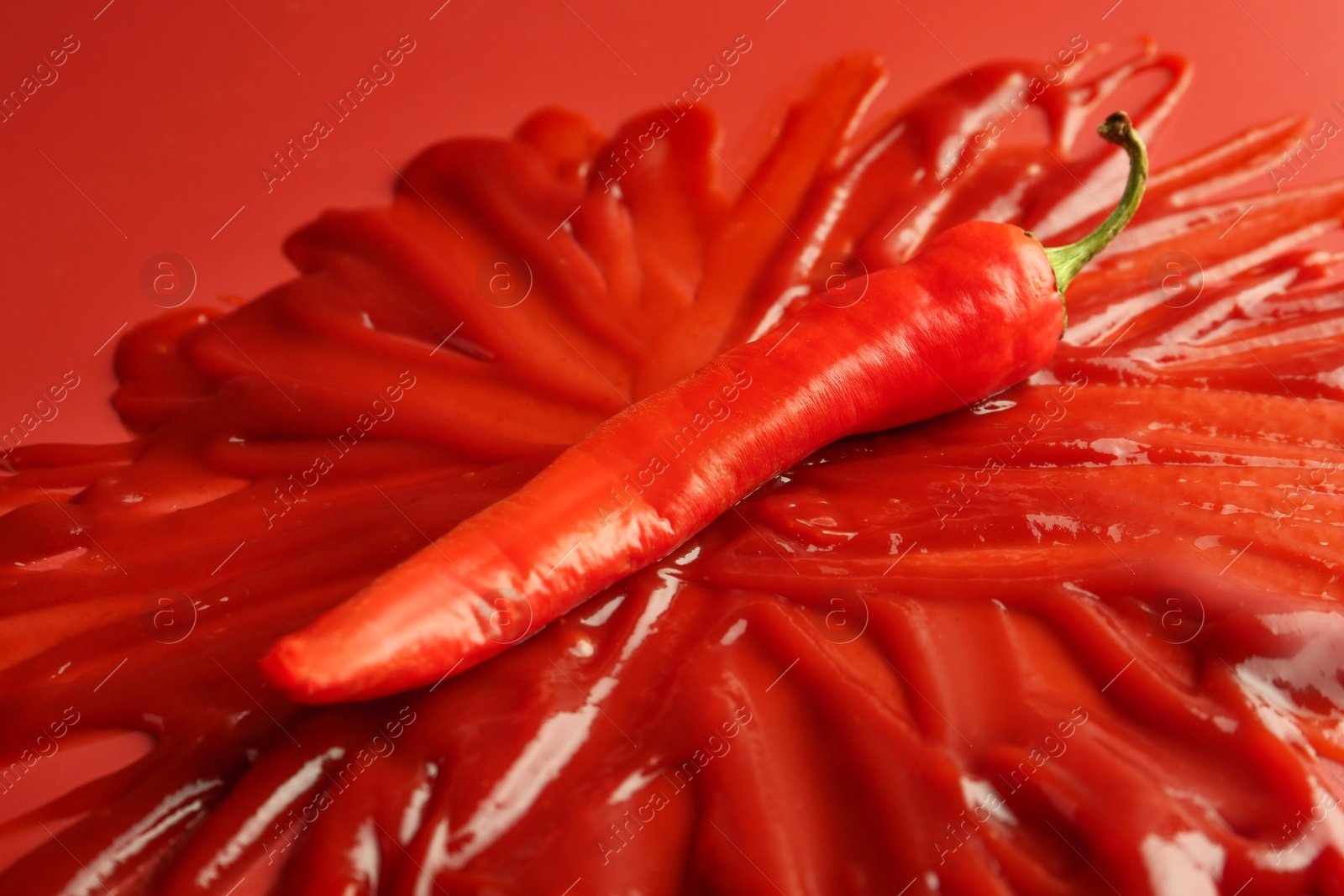 Photo of Tasty ketchup and chili pepper on red background, closeup