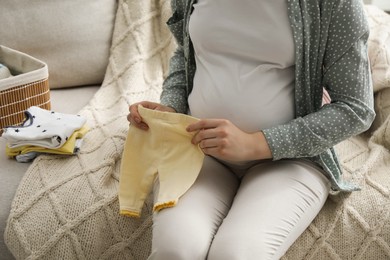 Photo of Pregnant woman with baby clothes on sofa at home, closeup