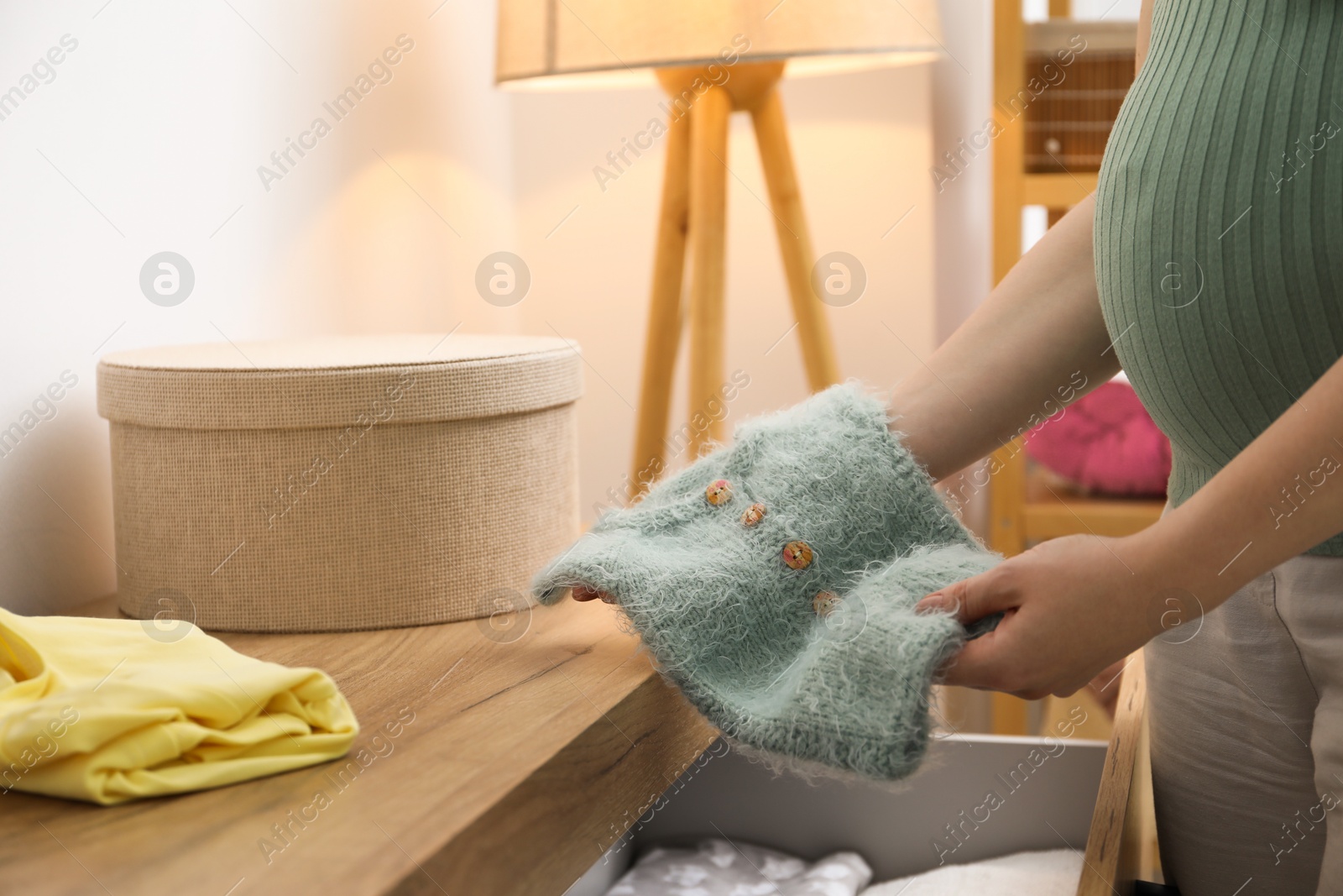 Photo of Pregnant woman with baby clothes at home, closeup