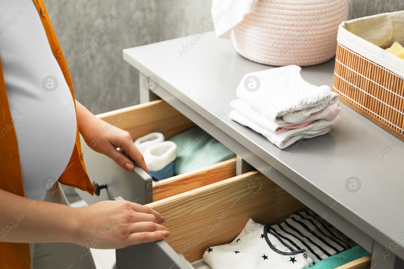 Photo of Pregnant woman with baby clothes at home, closeup