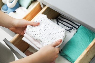 Photo of Woman putting baby clothes into drawer at home, closeup