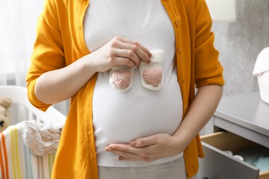 Photo of Pregnant woman with baby socks at home, closeup