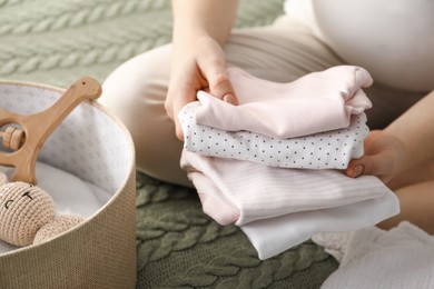 Photo of Pregnant woman with baby clothes on bed at home, closeup