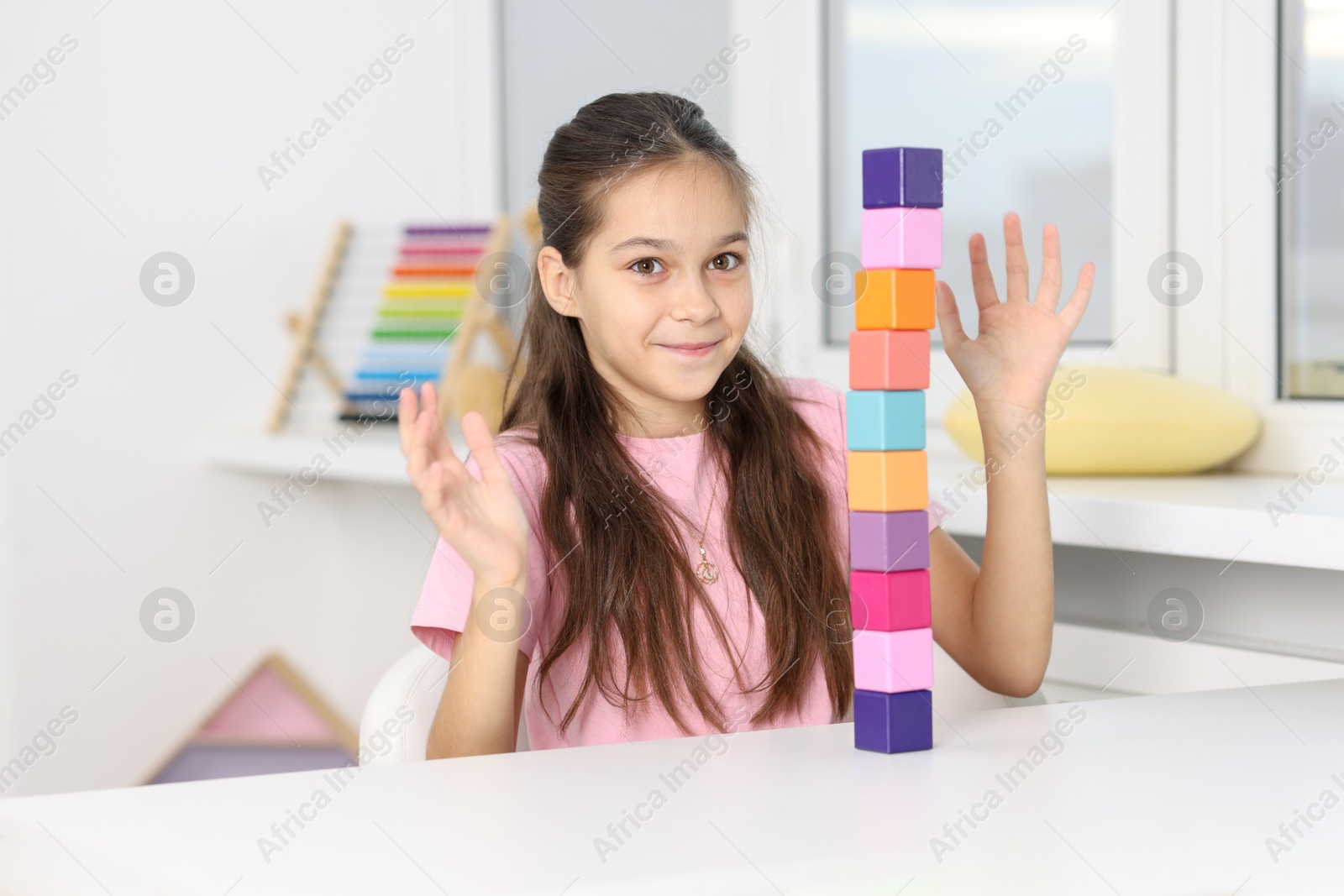 Photo of Happy girl with tower of colorful cubes at table indoors