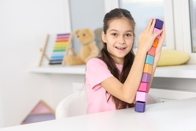 Photo of Happy girl with tower of colorful cubes at table indoors