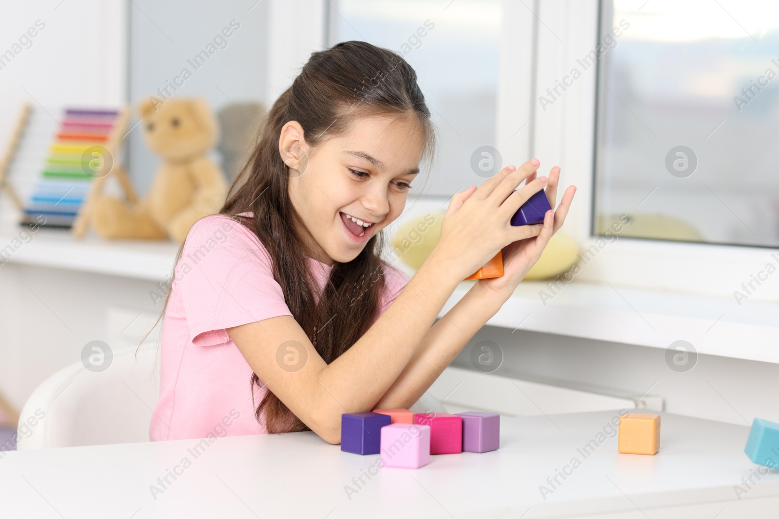 Photo of Happy girl with tower of colorful cubes at table indoors