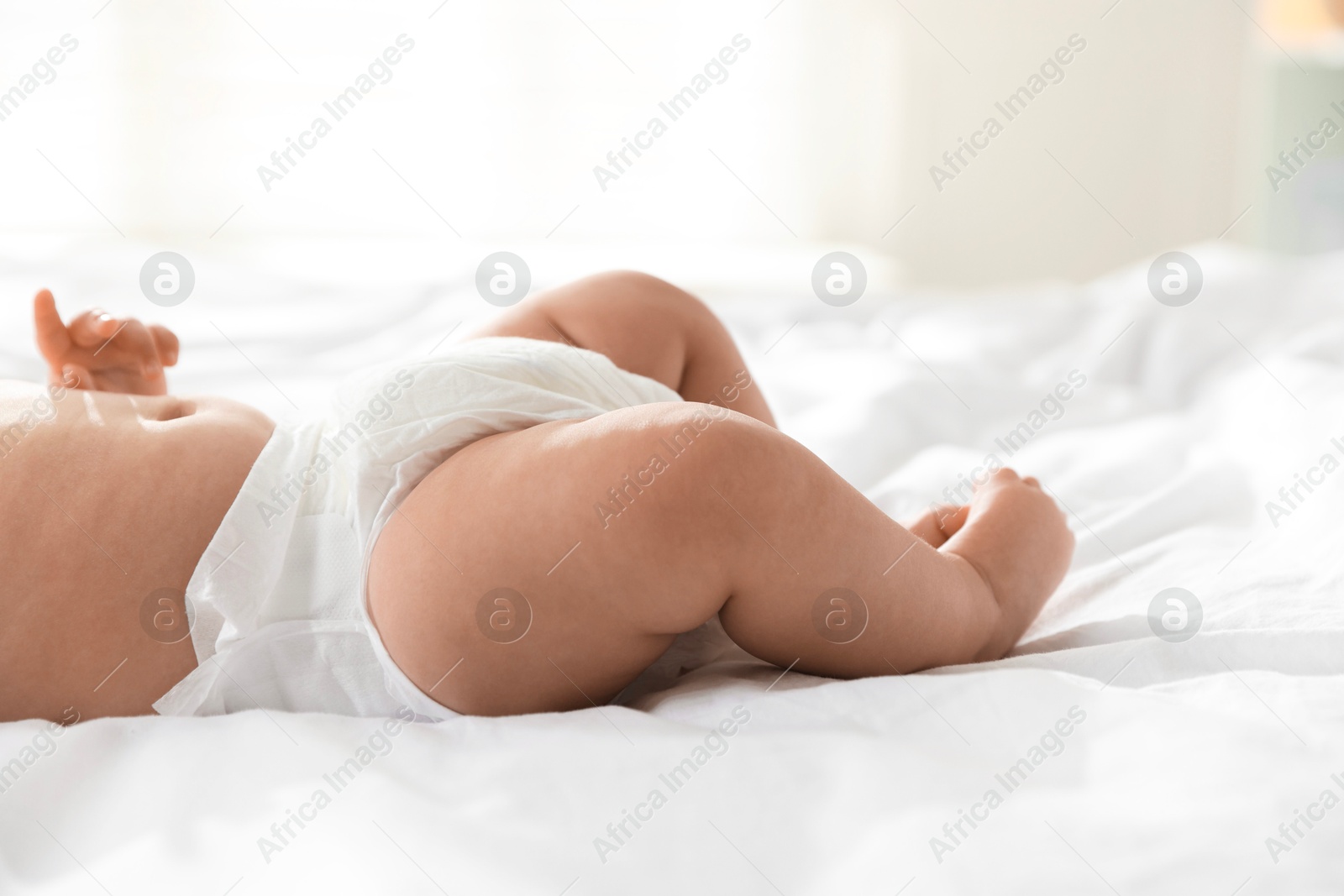 Photo of Cute little baby in diaper on bed indoors, closeup