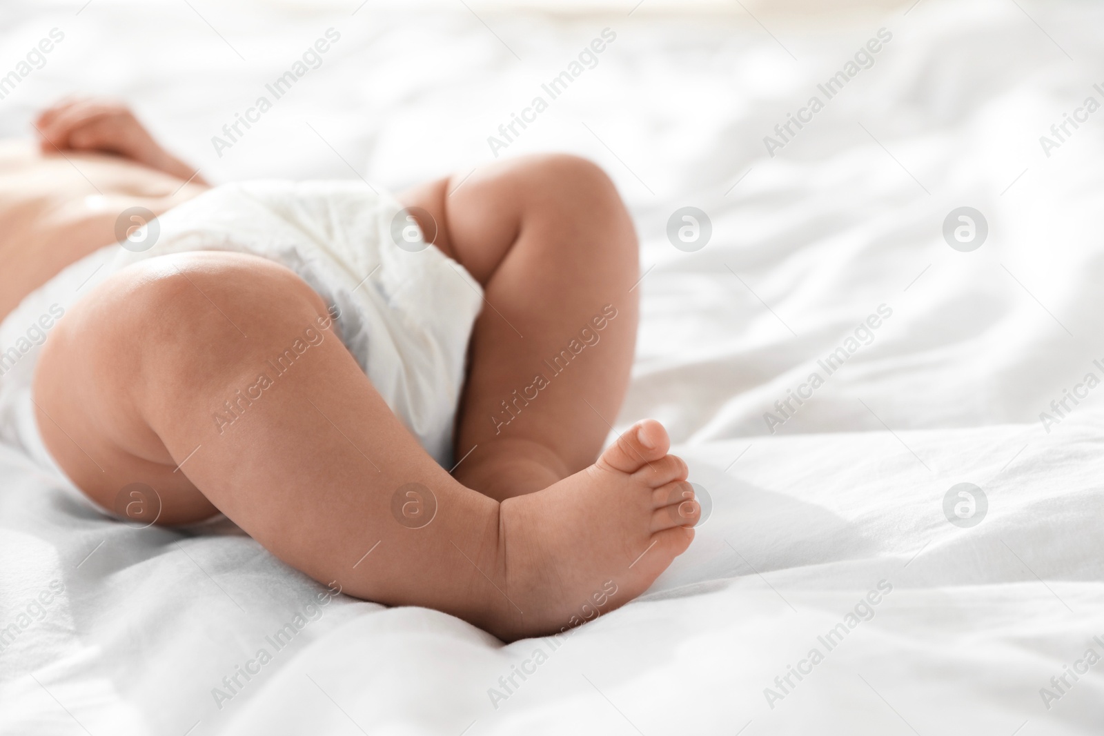 Photo of Cute little baby in diaper on bed, closeup