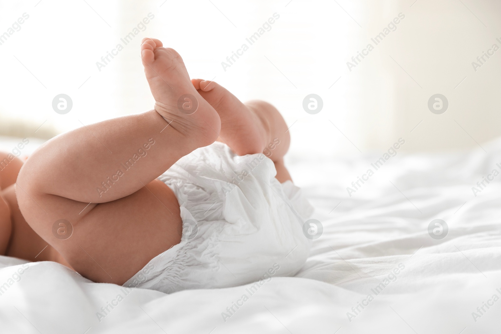 Photo of Cute little baby in diaper on bed indoors, closeup