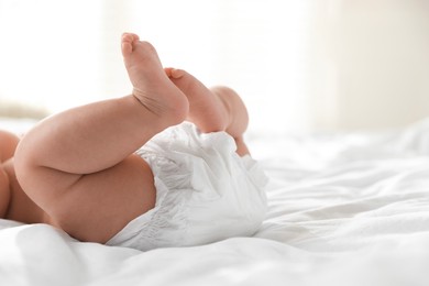 Photo of Cute little baby in diaper on bed indoors, closeup