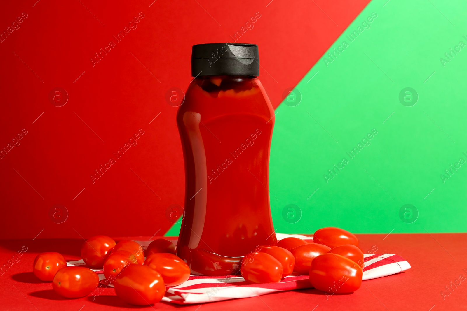 Photo of Bottle of ketchup and tomatoes on color background