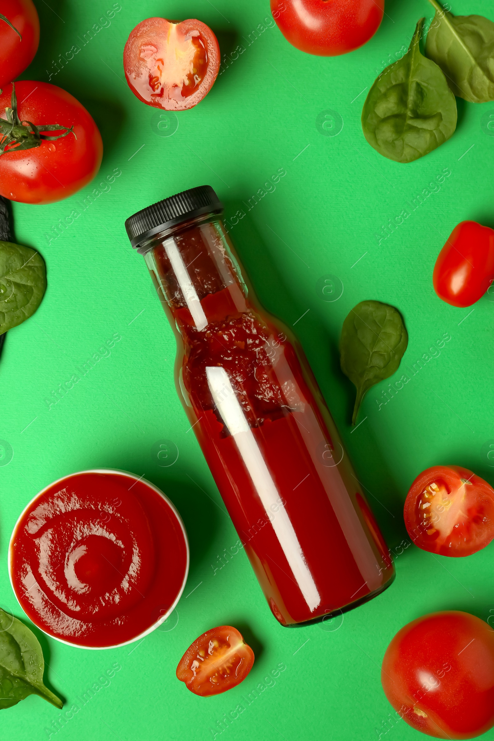 Photo of Ketchup, tomatoes and spinach on green background, flat lay