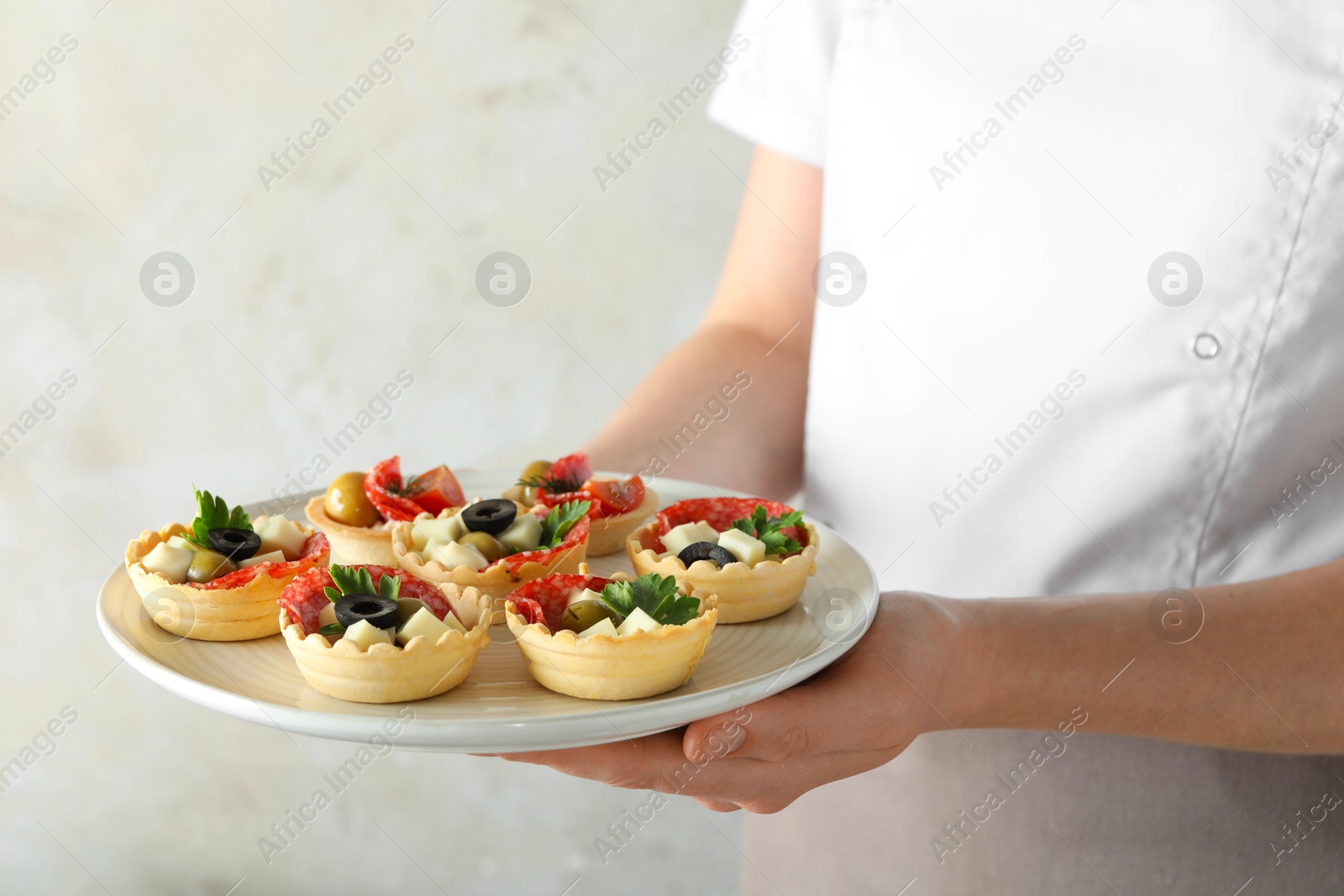 Photo of Woman holding plate with tasty canapes on light grey background, closeup