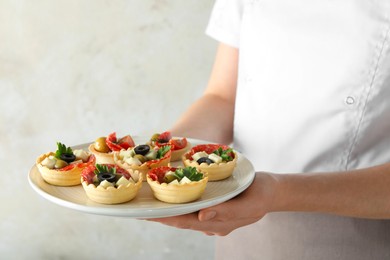 Photo of Woman holding plate with tasty canapes on light grey background, closeup