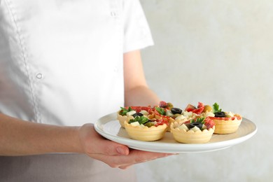 Photo of Woman holding plate with tasty canapes on light grey background, closeup