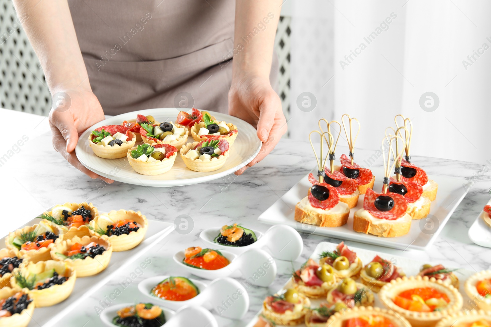 Photo of Woman with many different tasty canapes at white marble table, closeup