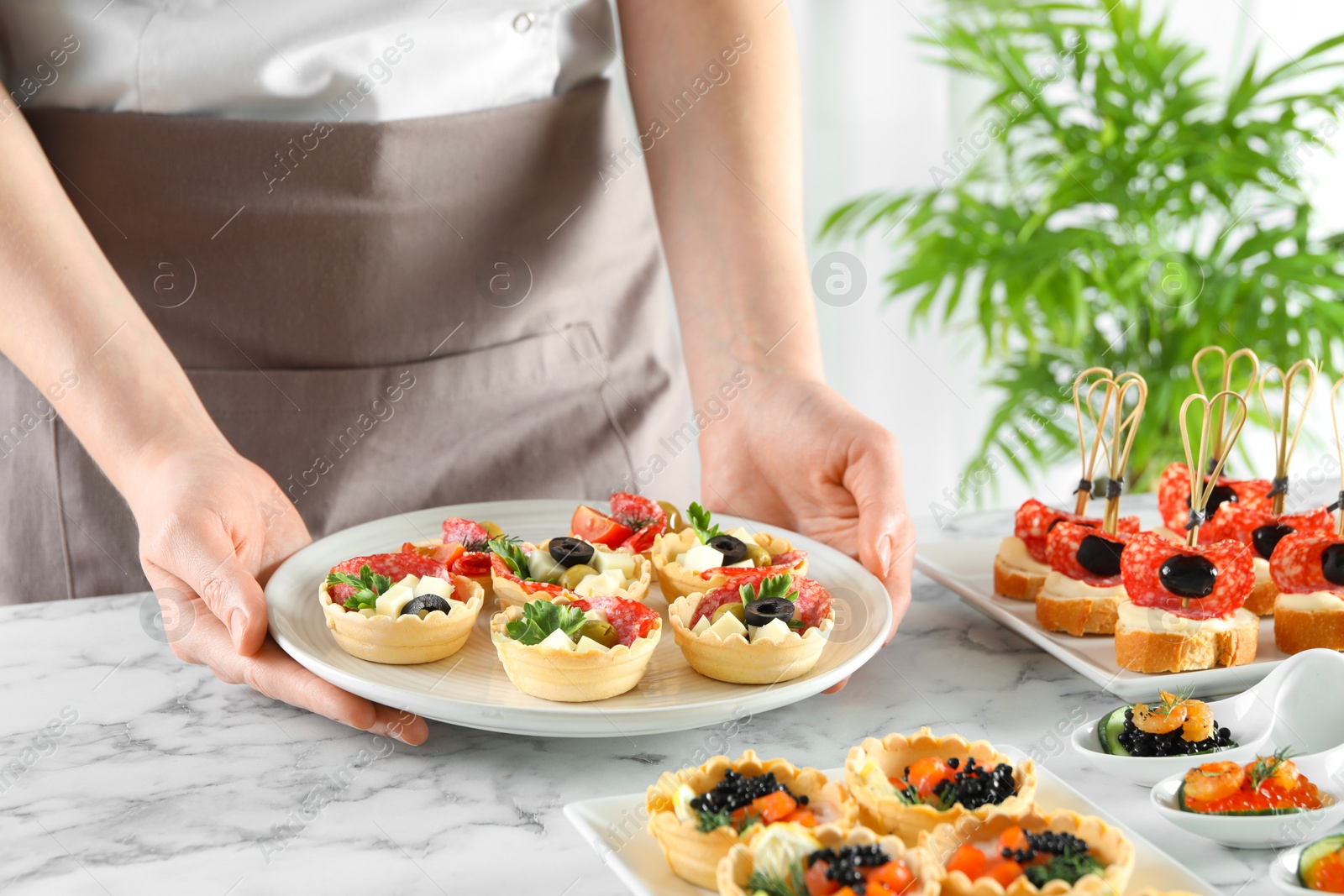 Photo of Woman with many different tasty canapes at white marble table, closeup