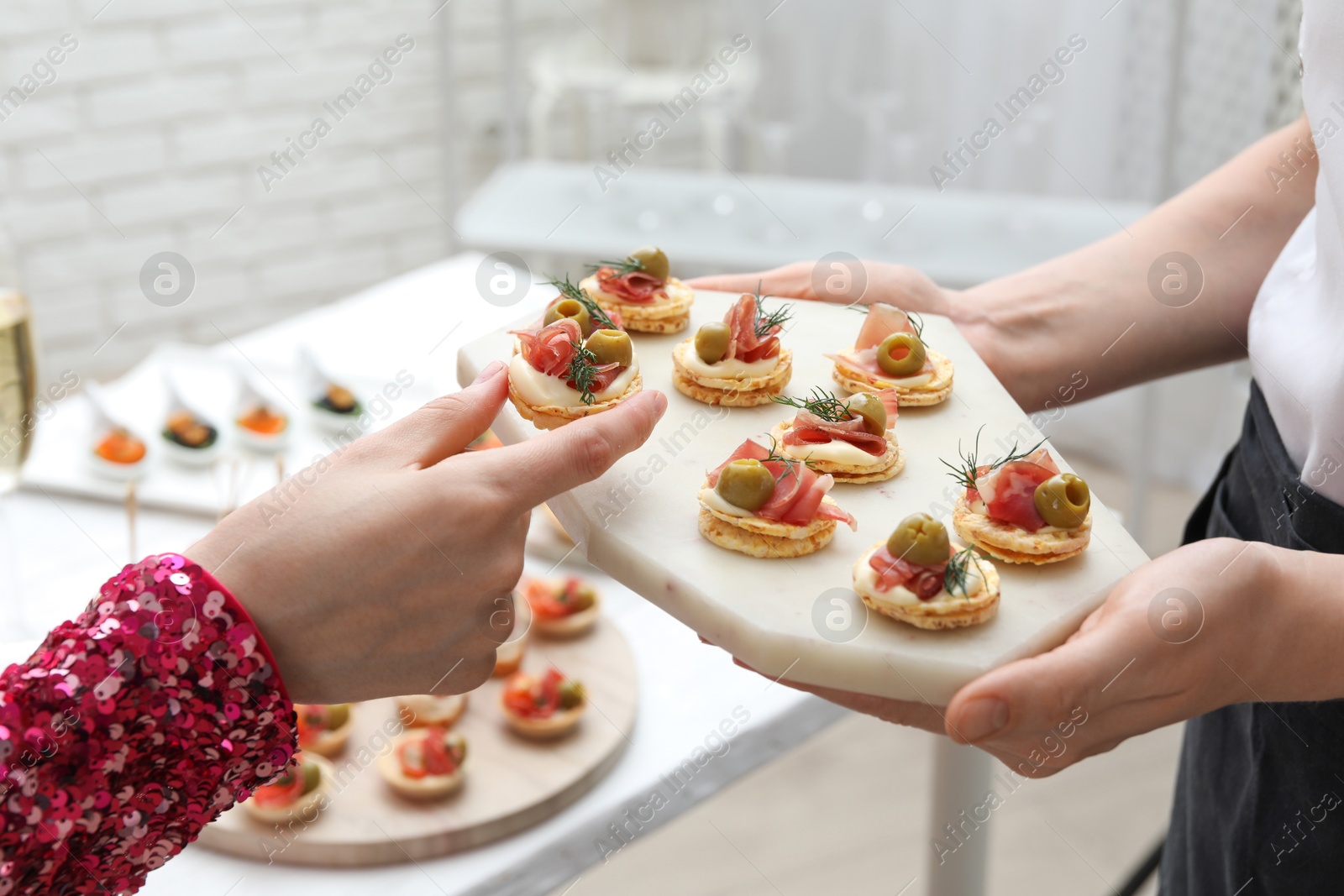 Photo of Woman taking tasty canape from waiter with board indoors, closeup