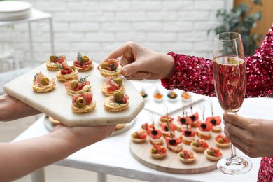 Photo of Woman taking tasty canape from waiter with board indoors, closeup