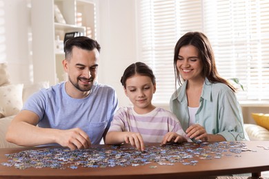 Photo of Happy parents and their daughter solving puzzle together at wooden table indoors