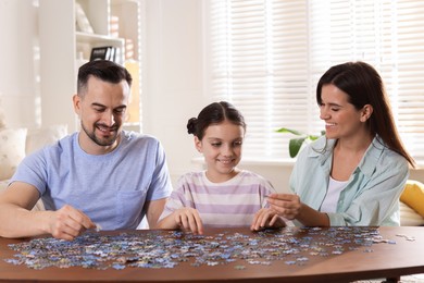 Photo of Happy parents and their daughter solving puzzle together at wooden table indoors