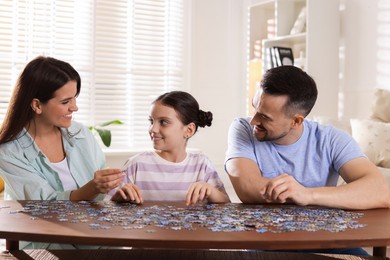 Photo of Happy parents and their daughter solving puzzle together at wooden table indoors