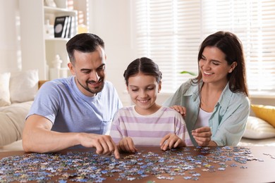 Photo of Happy parents and their daughter solving puzzle together at wooden table indoors