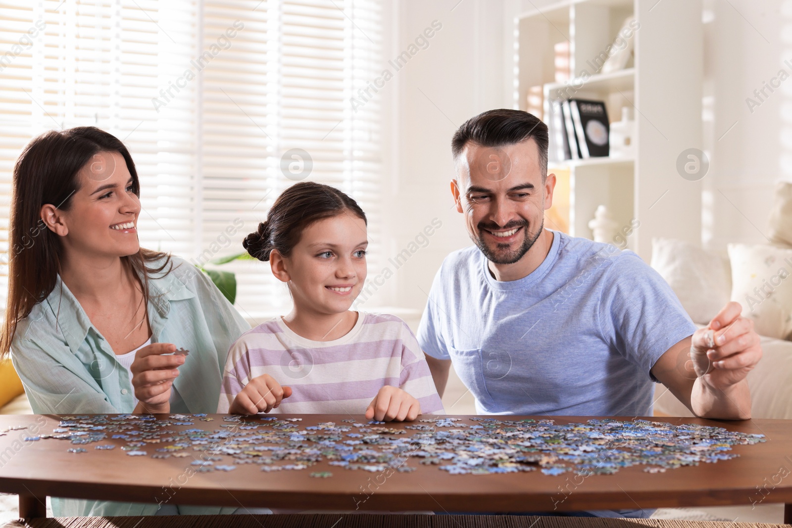 Photo of Happy parents and their daughter solving puzzle together at wooden table indoors