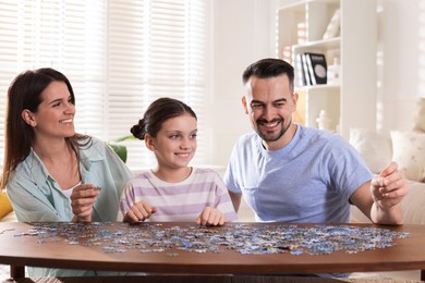 Photo of Happy parents and their daughter solving puzzle together at wooden table indoors