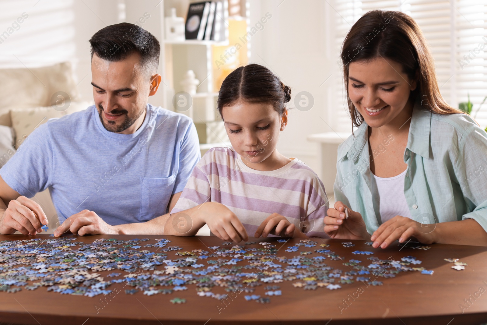 Photo of Happy parents and their daughter solving puzzle together at wooden table indoors