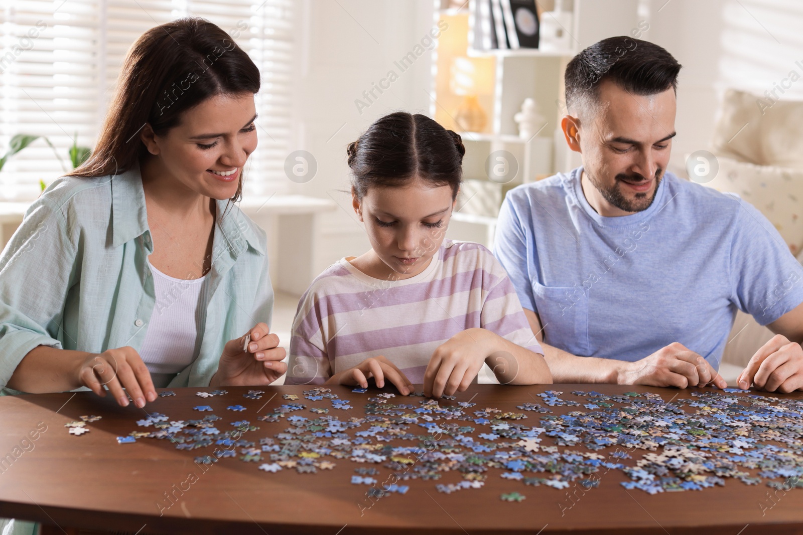 Photo of Happy parents and their daughter solving puzzle together at wooden table indoors