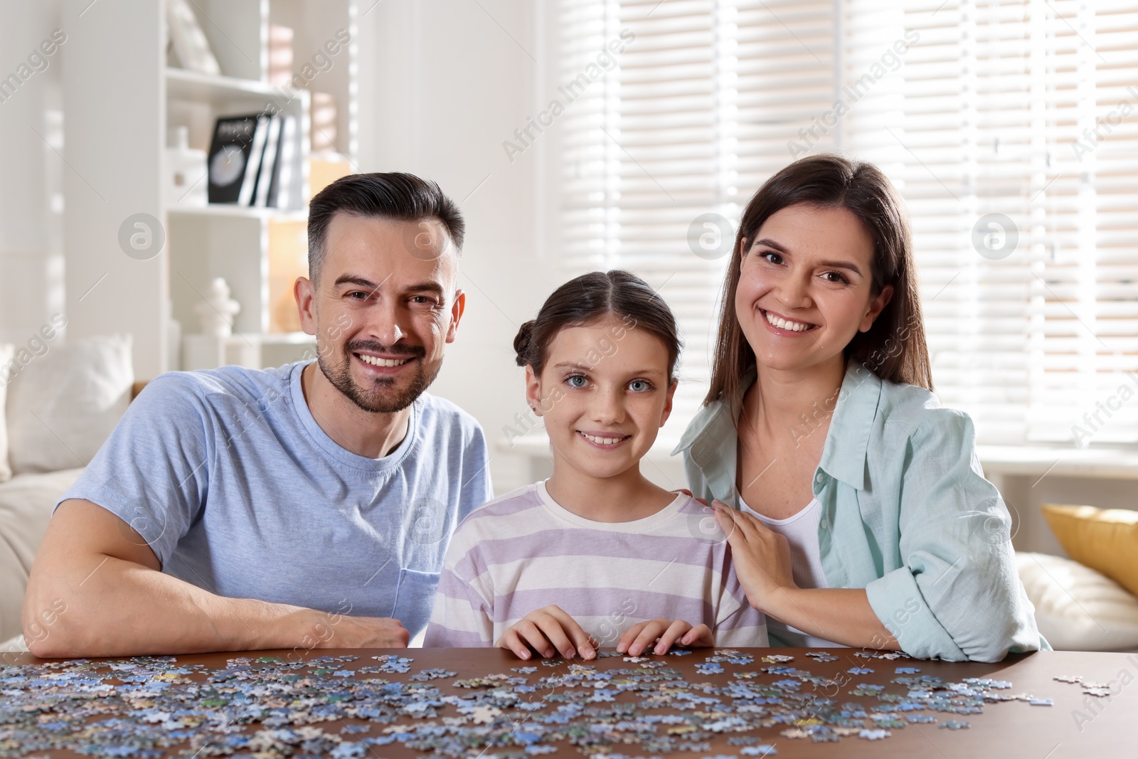 Photo of Happy parents and their daughter solving puzzle together at wooden table indoors