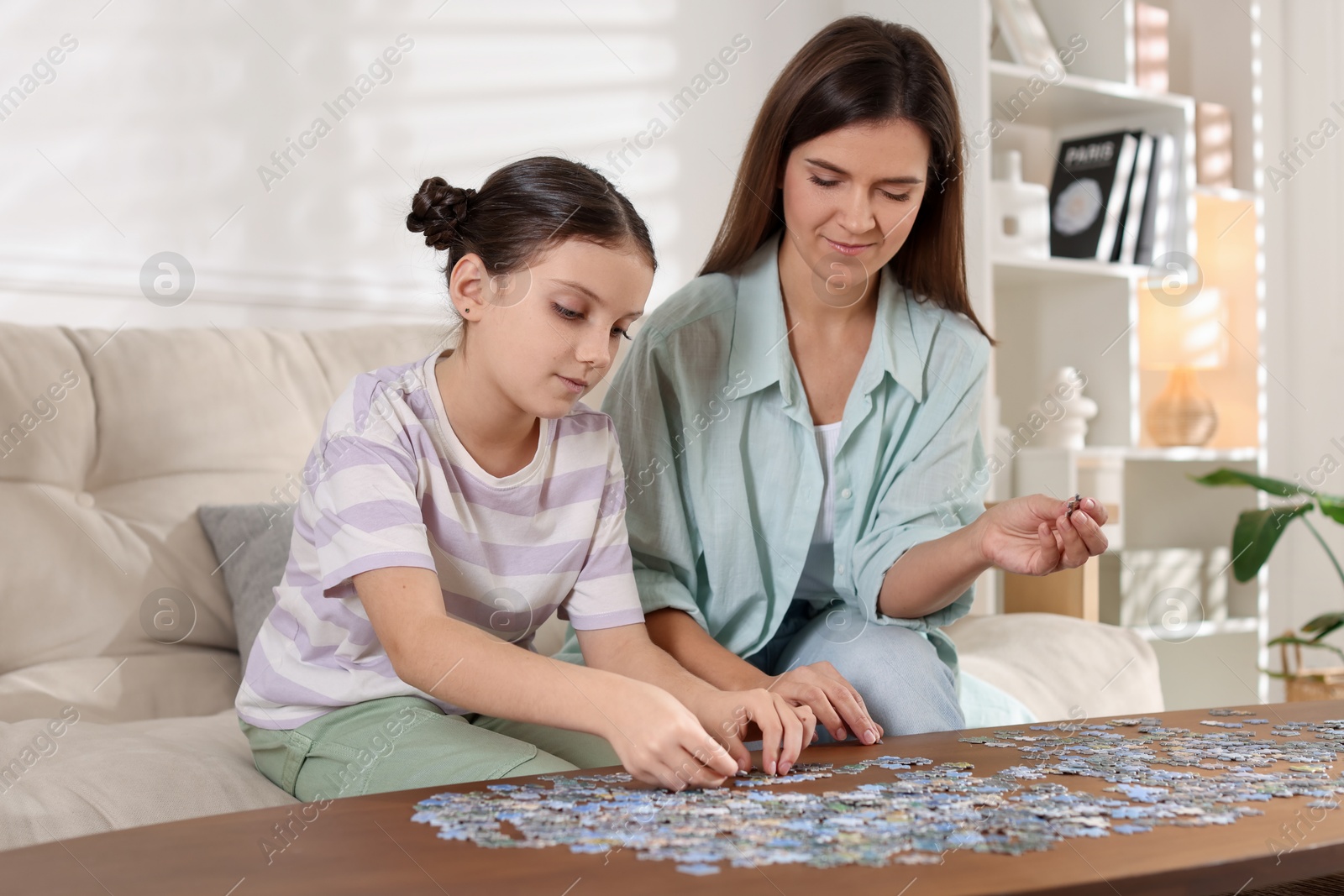 Photo of Happy mother and her daughter solving puzzle together at wooden table indoors