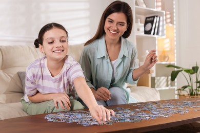 Photo of Happy mother and her daughter solving puzzle together at wooden table indoors